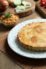 Chicken pie with cottage cheese, tomatoes, onion and olives on wooden table and white plate.