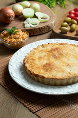 Chicken pie with cottage cheese, tomatoes, onion and olives on wooden table and white plate.