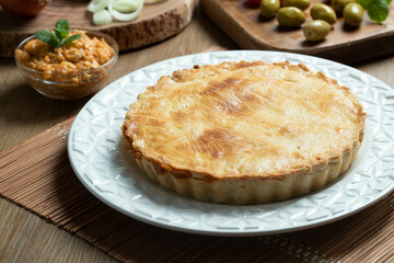 Chicken pie with cottage cheese, tomatoes, onion and olives on wooden table and white plate.