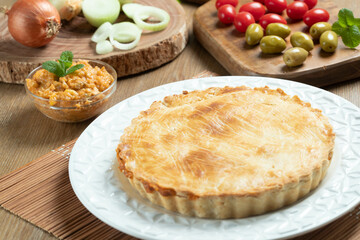 Chicken pie with cottage cheese, tomatoes, onion and olives on wooden table and white plate.