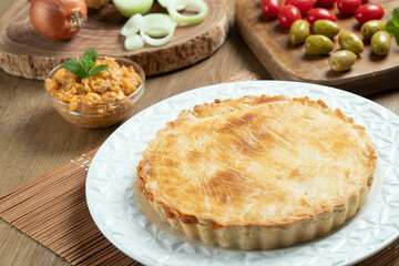 Chicken pie with cottage cheese, tomatoes, onion and olives on wooden table and white plate.
