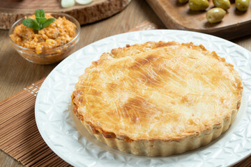 Chicken pie with cottage cheese, tomatoes, onion and olives on wooden table and white plate.