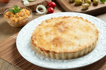 Chicken pie with cottage cheese, tomatoes, onion and olives on wooden table and white plate.