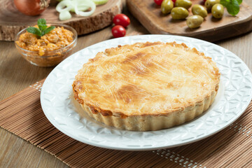 Chicken pie with cottage cheese, tomatoes, onion and olives on wooden table and white plate.