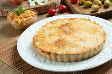 Chicken pie with cottage cheese, tomatoes, onion and olives on wooden table and white plate.
