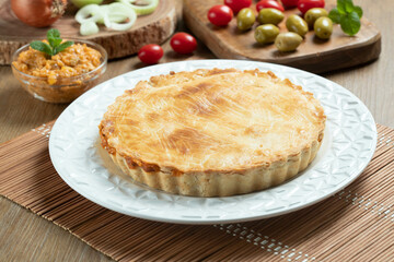Chicken pie with cottage cheese, tomatoes, onion and olives on wooden table and white plate.