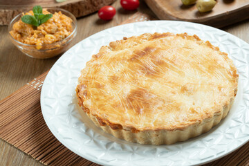 Chicken pie with cottage cheese, tomatoes, onion and olives on wooden table and white plate.