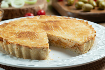Chicken pie with cottage cheese, tomatoes, onion and olives on wooden table and white plate.