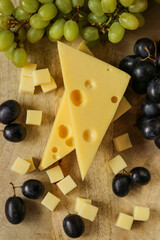 Cheese cut with fruits.Mazdar cheese triangles, gouda cheese cubes and black and green grapes.Cheese with grapes berries on wooden board background.milk fat and Milk products.