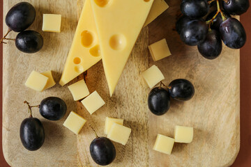 Mazdar cheese triangles, gouda cheese cubes and black grapes.Cheese with grapes berries on wooden board background.milk fat and Milk products.