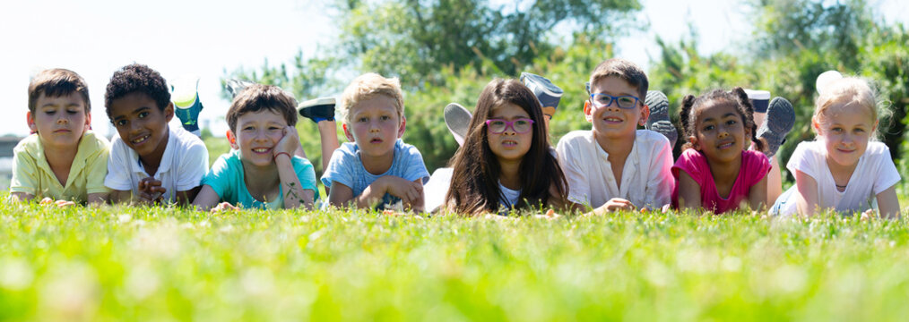 Group of happy children resting on grass and smiling together in park