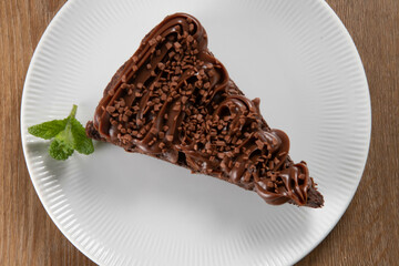 Piece of Chocolate Brownie Slice with Strawberry and Chocolate Icing. Wooden table with mint and chocolate chips in the background. Top view