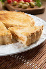 Close up piece of Chicken pie with cottage cheese, tomatoes, onion and olives on wooden table and white plate