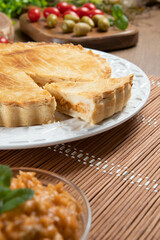 Close up piece of Chicken pie with cottage cheese, tomatoes, onion and olives on wooden table and white plate