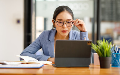 Portrait of smiling pretty young Asian businesswoman in glasses sitting on workplace