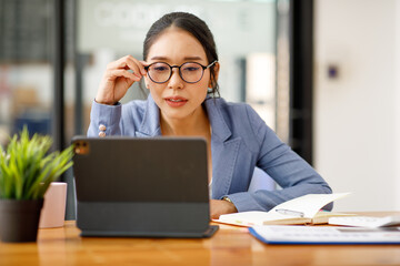 Fototapeta premium Portrait of smiling pretty young Asian businesswoman in glasses sitting on workplace