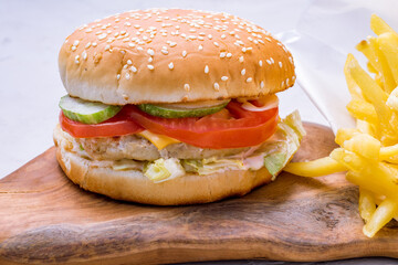 Burger with chicken, vegetables and french fried on the board macro close up