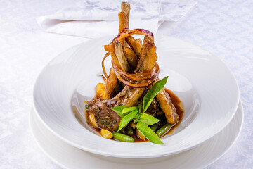 kebab from a rack of lamb with red onion and baby potatoes on a white plate