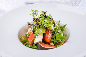 Salad with cheese and figs with flambe fruits and greens on a white plate macro close up