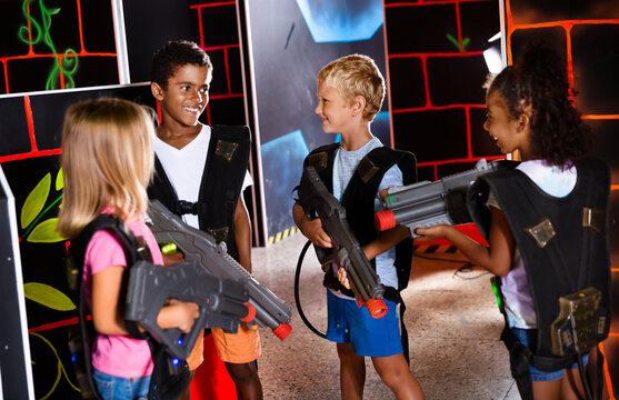 Joyful teens aiming laser guns at other players during lasertag game in dark room. High quality photo