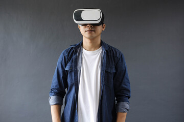 Young man using Virtual Reality googles on dark grey background.