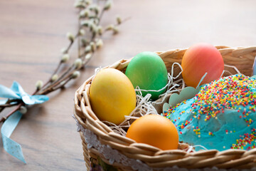 Congratulatory Easter background. Easter eggs and Easter cake in a wicker basket and a willow branch on the table.