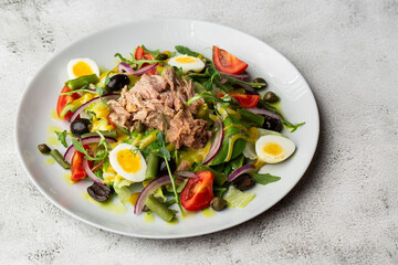 French salad Nicoise with tuna, egg, green beans, tomatoes, olives, lettuce, onions and anchovies on a white background. Healthy food