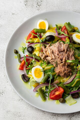 French salad Nicoise with tuna, egg, green beans, tomatoes, olives, lettuce, onions and anchovies on a white background. Healthy food