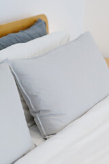 Wooden bed with white blanket and gray pillows in a modern apartment. Soft focus image.