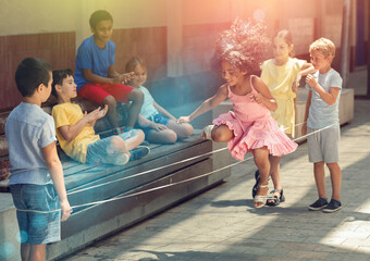 Happy peruvian little girl jumping game by rubber band with european friends on the street