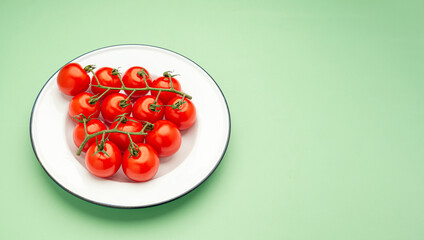 Group of red ripe fresh cherry tomatoes on a white dish over a green background