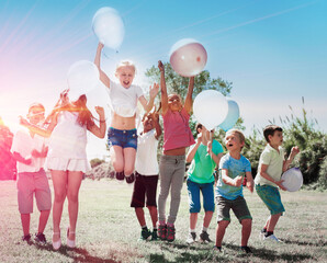 Group of happy children holding ballons and jumping together in park