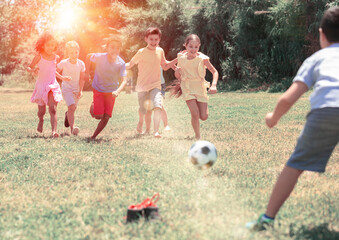 Group of happy schoolchildren playing football together in park