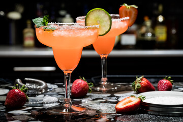 Two strawberry margaritas on a bar, against a dark background. - obrazy, fototapety, plakaty
