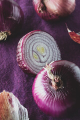 Whole and cut red onions against a purple background. 