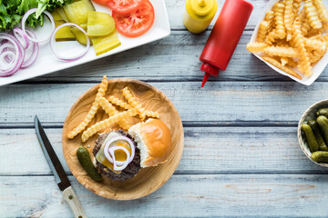 A cheeseburger slider on a wooden plate served with french fries.