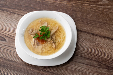 Tasty chicken soup bouillon with noodles, chicken meat, dill and parsley in a white bowl. Isolated on wooden background. Healthy meal menu.