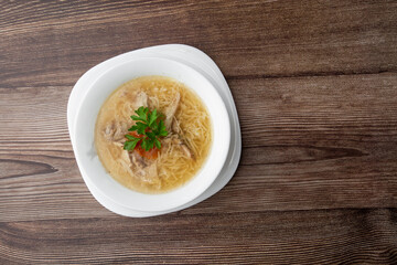 Tasty chicken soup bouillon with noodles, chicken meat, dill and parsley in a white bowl. Isolated on wooden background. Healthy meal menu.