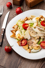 A Caesar salad with grilled chicken breasts, lettuce, croutons, eggs, cherry tomatoes, dressed with Parmesan cheese and sauce. On wooden background.