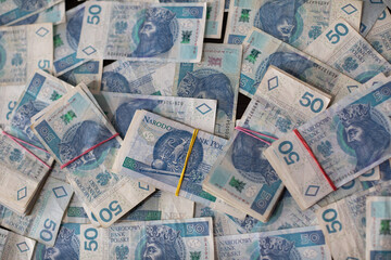 A file of banknotes lies on a scattering of fifty Polish zloty bills.
