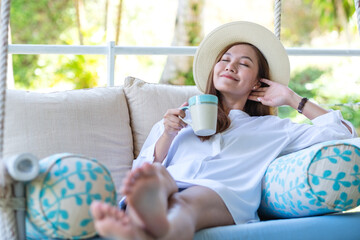 Portrait image of a young woman with hat drinking coffee while relaxing and laying down on swing...