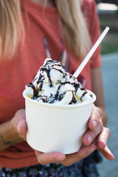 Woman holding takeaway cup with ice cream or frozen yogurt on summer day. Food or healthy delicious dessert in heat weather, summertime. Close up, vertical