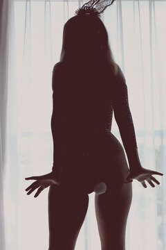 Silueta de una joven mujer adulta usando lencer&iacute;a, disfraz sensual con orejas y cola de conejita, tacones altos y m&aacute;scara piel suavemente contraluz al atardecer creando en una atm&oacute;sfera de misterio