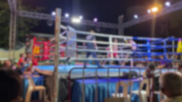 Blurred motion background youth amateur Muay Thai Boxing match red corner boxer knockout punch. Thai boxing fighting on stage ringside view at night time outdoor arena spotlight