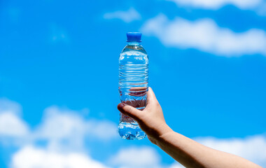 A girl holds a bottle of drinking water in her hand against a blue sky background
