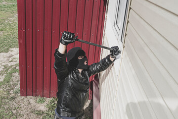 A criminal concept. Burglary. Thief in balaclava breaking glass of window to enter the house