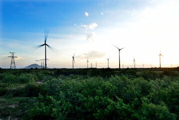 Wind farm or wind park, with high wind turbines under the blue sky for generation electricity with...