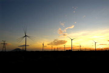 Wind farm or wind park, with high wind turbines in the setting sun for generation electricity with copy space. Green energy concept to reduce climate change and global warming
