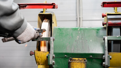 a factory worker sharpens a large drill on a grinder