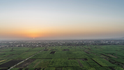 Dawn over the Nile Valley. The sun rises in a pinkish sky. Green cultivated plantations, village houses, riverbed are visible. View from above. Egypt. Luxor